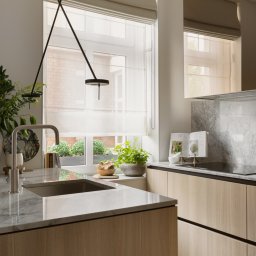 EMITOM design & build S.C. - Jasna kuchnia z drewnianymi szafkami, marmurowym blatem i backsplash, oświetlona nowoczesną lampą wiszącą i światłem dziennym z okna z widokiem na zielony ogród.