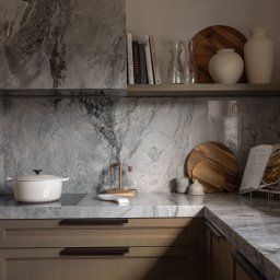 EMITOM design & build S.C. - Nowoczesna kuchnia z marmurowym blatem i backsplashiem, drewniane szafki z minimalistycznymi uchwytami, biały garnek na płycie, dekoracyjne naczynia i książki na półce.