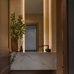 EMITOM design & build S.C. - Nowoczesna łazienka z marmurową umywalką, podświetlanym lustrem i teksturowanymi ścianami, widok zza uchylonych drzwi.