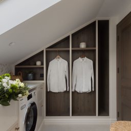 EMITOM design & build S.C. - Nowoczesna pralnia w skosach poddasza z białą pralką Miele, zabudową szaf z półkami i wieszakami na koszule oraz bukietem białych kwiatów.