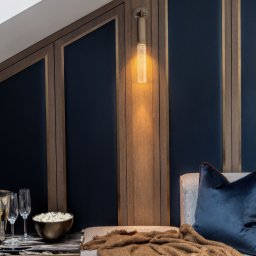 EMITOM design & build S.C. - Nowoczesna sypialnia na poddaszu z zabudową z drewnianymi panelami i granatowymi wstawkami, oświetlona podłużnym kinkietem, z dekoracyjnym stolikiem nocnym, szampanem i popcornem.