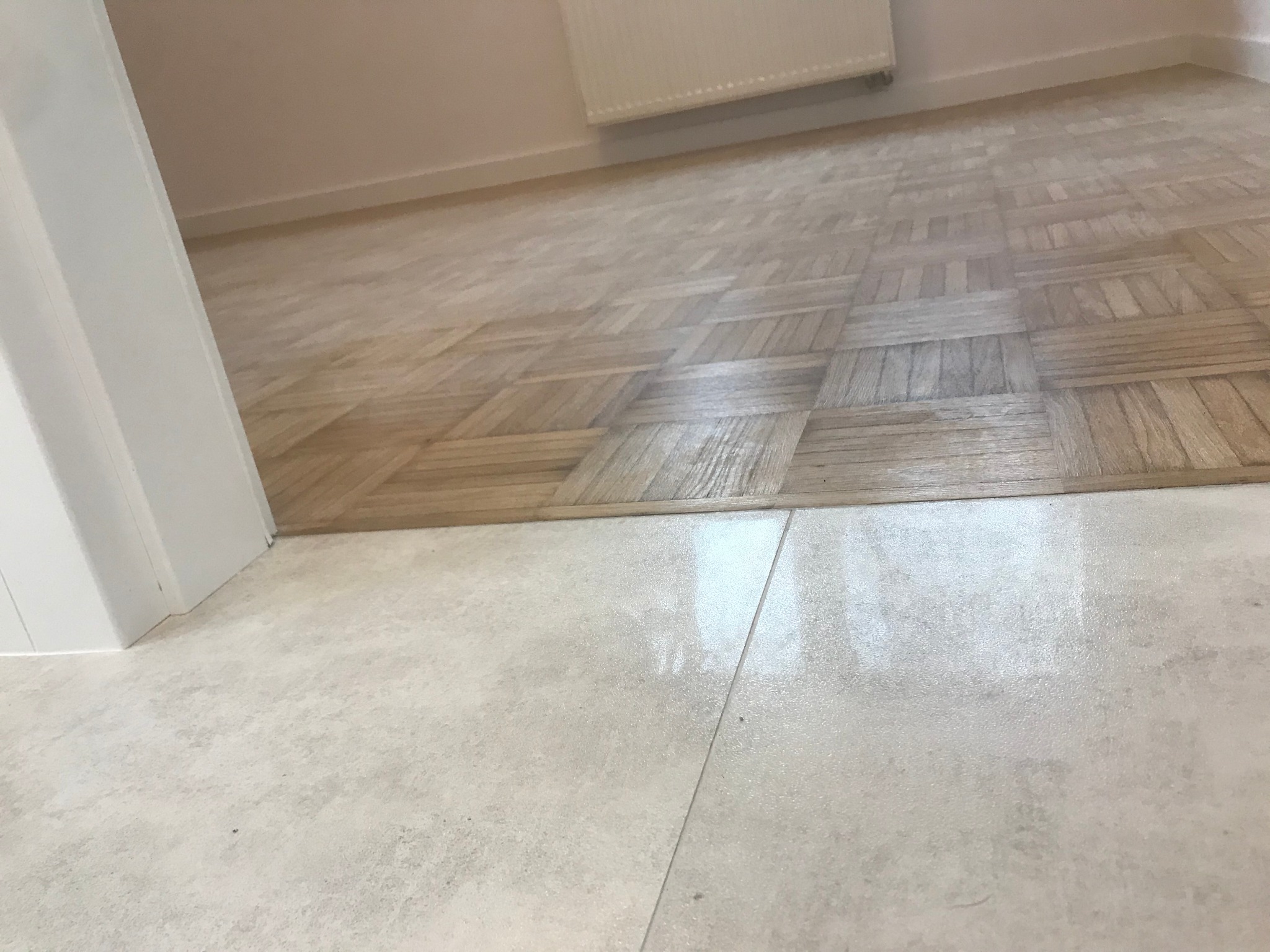 Połączenie parkietu w jodełkę z jasnymi, matowymi płytkami ceramicznymi w przejściu między pomieszczeniami, bez listwy progowej.