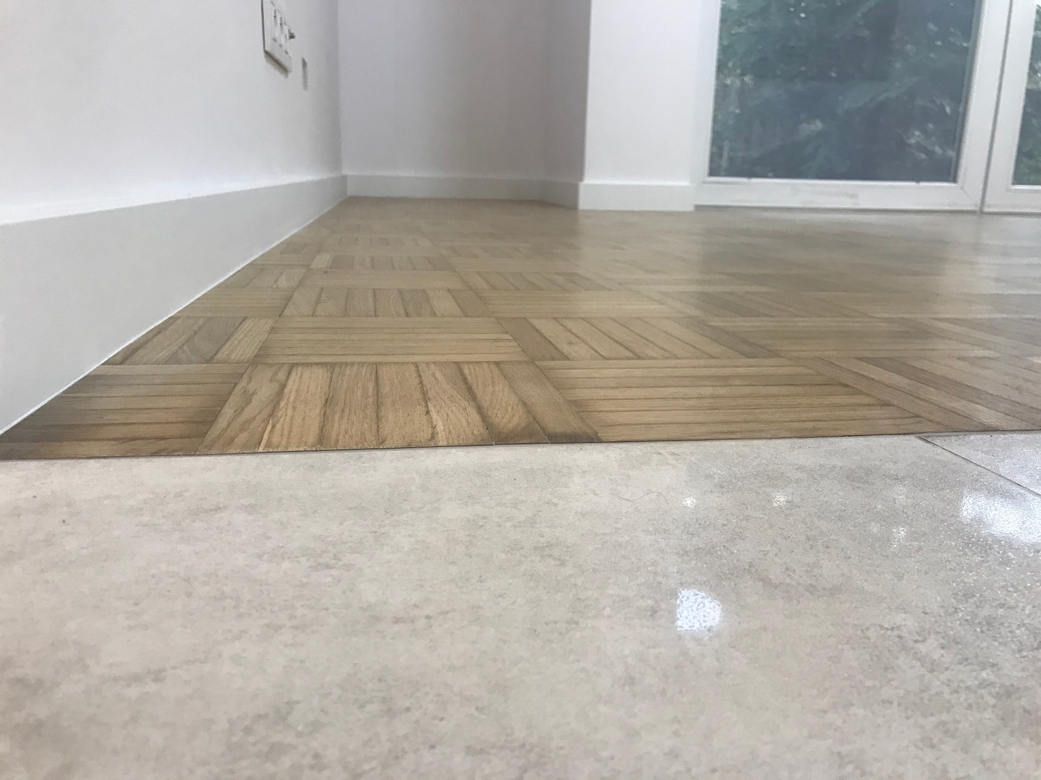 Połączenie parkietu ułożonego w kwadraty z jasnym gresem w jednym poziomie, bez listwy progowej, w pokoju dziennym z widokiem na okno.