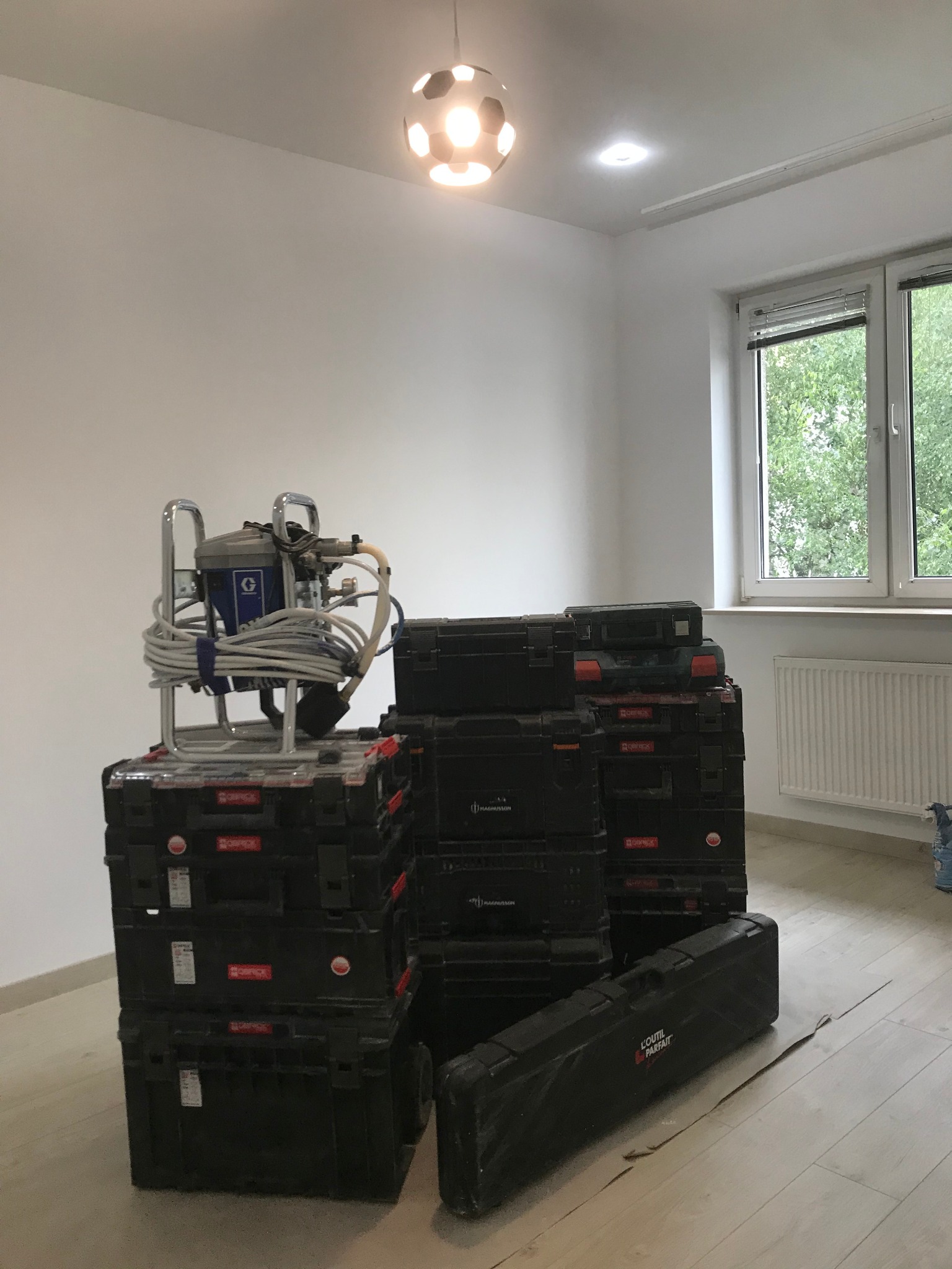 Sprzęt do malowania natryskowego na stercie czarnych skrzyń narzędziowych w jasnym pokoju z oknem i lampą w kształcie piłki.