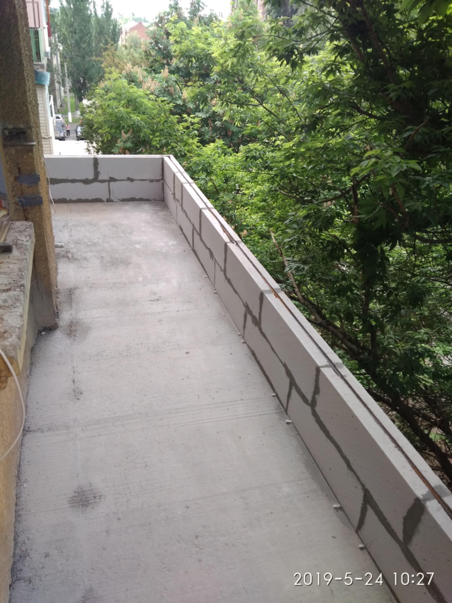 Surowy balkon z betonu komórkowego w trakcie budowy, widok na zieleń drzew