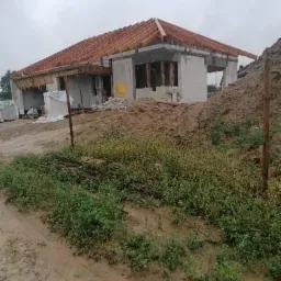 Surowy stan domu murowanego w trakcie budowy, widoczne ściany z betonu komórkowego, konstrukcja dachu z drewnianych łat i kontrłat, oraz ziemia i roślinność na pierwszym planie w pochmurny dzień.