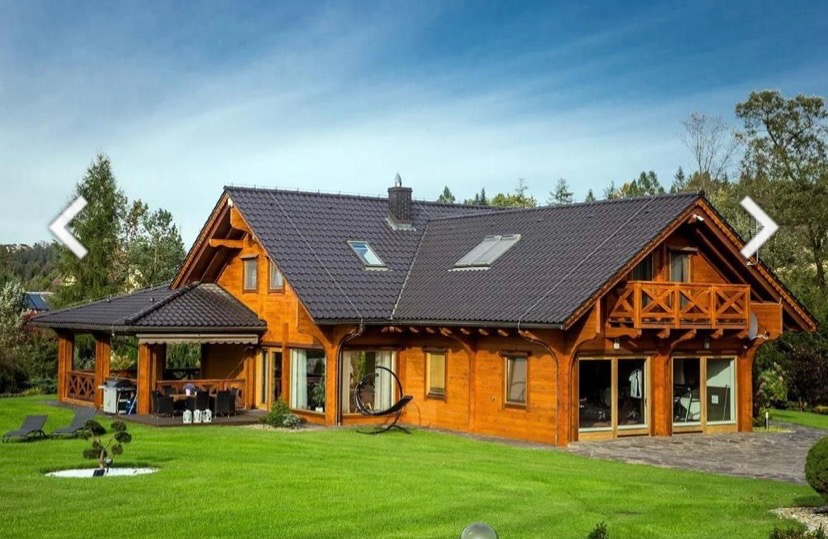 Dwukondygnacyjny dom z bali z ciemnym dachem i werandą, widok z zadbanego trawnika w słoneczny dzień.