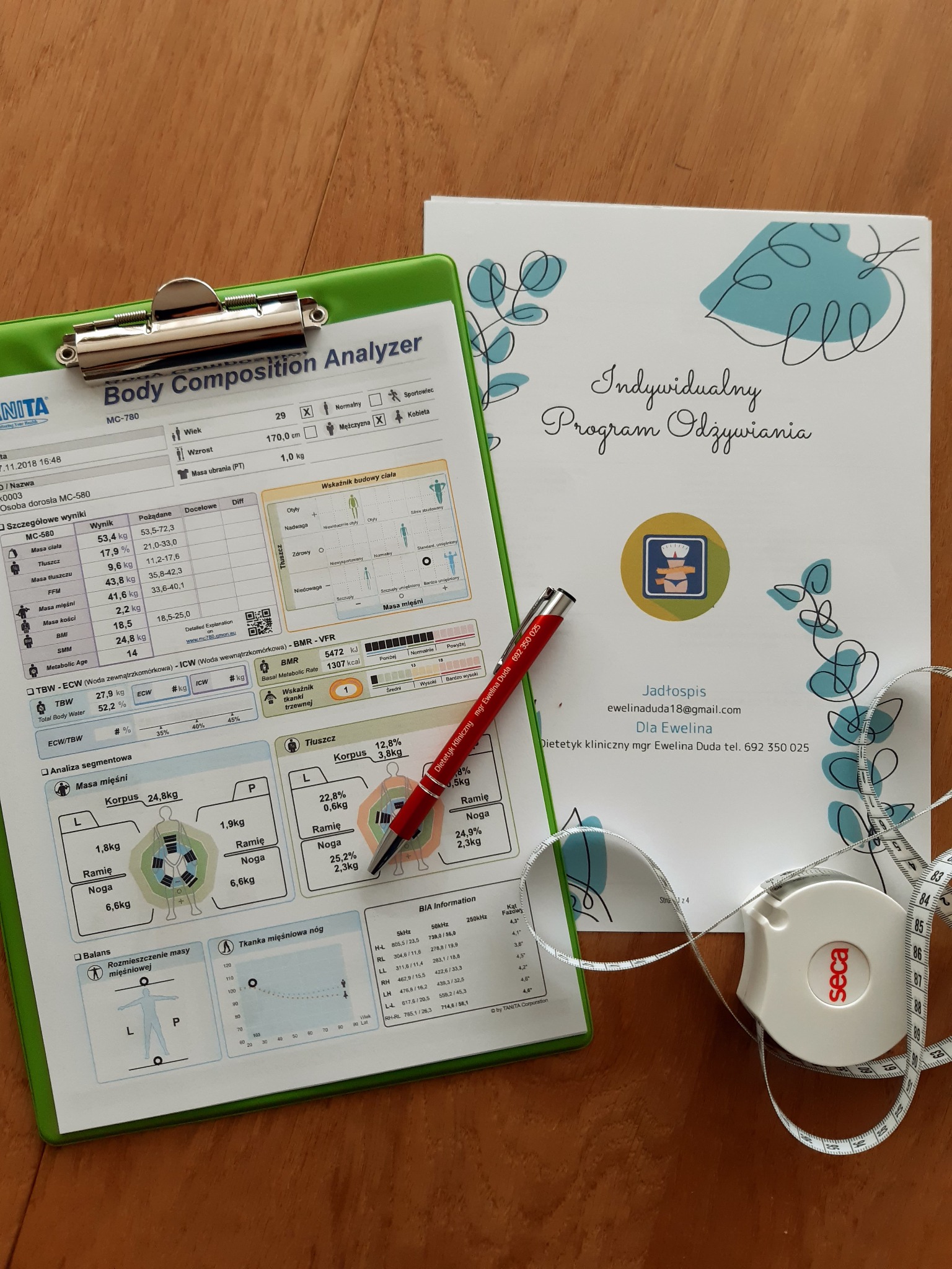 Analiza składu ciała na zielonym podkładzie, obok miarka Seca i wizytówka z danymi kontaktowymi, indywidualny program odżywiania