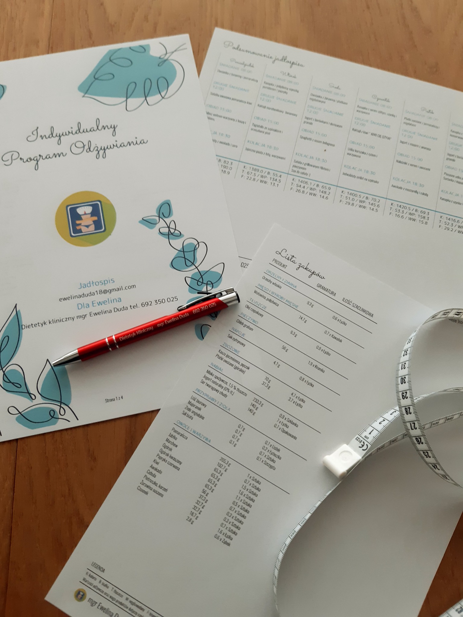 Program żywieniowy z listą zakupów, długopisem i miarką krawiecką na drewnianym stole.