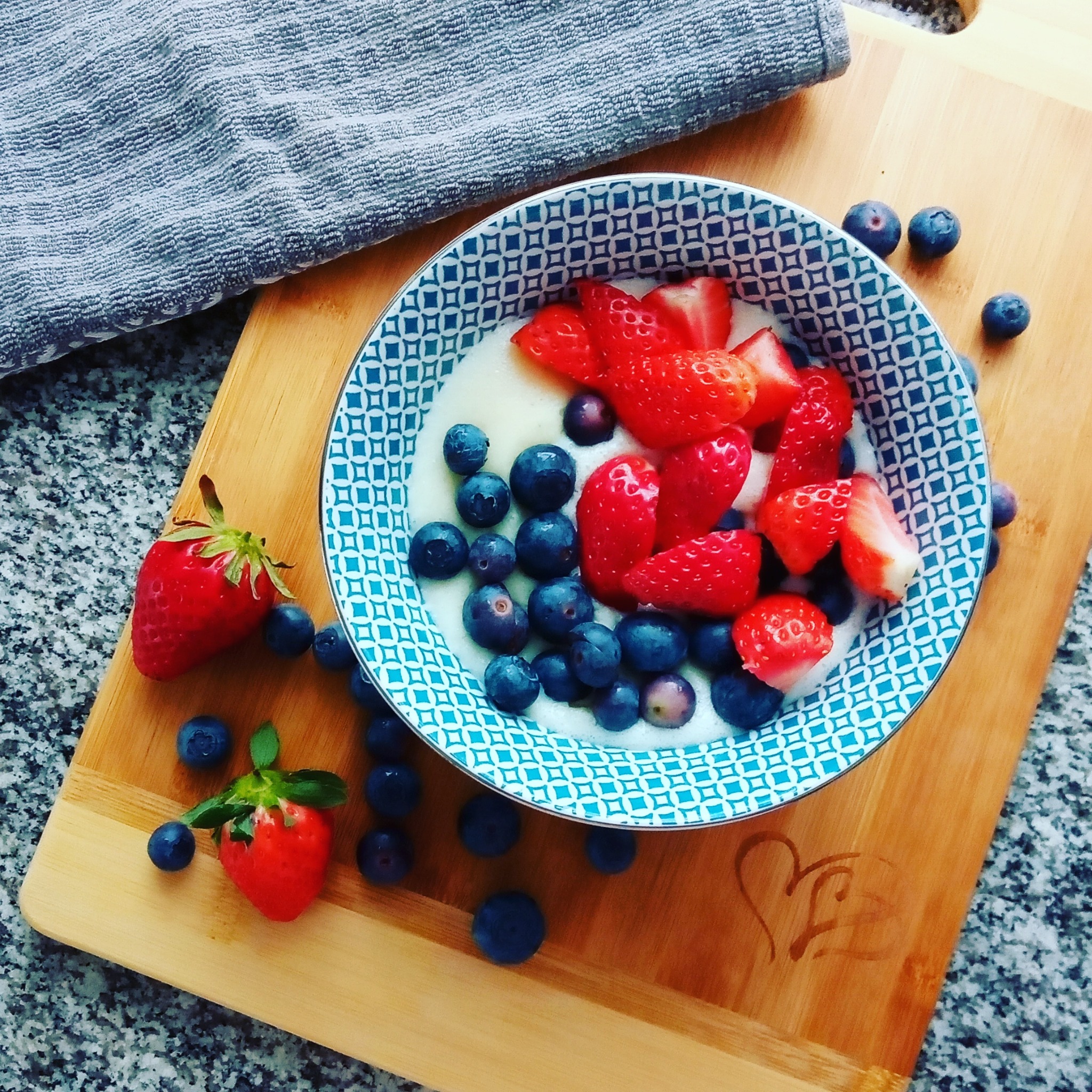 Zdjęcie z góry miseczki z jogurtem, truskawkami i borówkami na drewnianej desce z wyrytym sercem, widok z Milicza.
