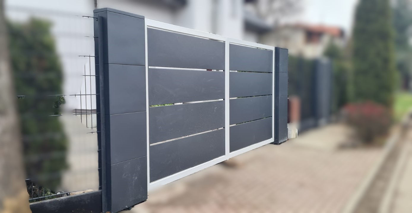 Nowoczesna brama przesuwna z poziomymi panelami w kolorze grafitowym, osadzona na masywnych, ciemnych słupkach z dekoracyjnymi płytkami, widoczna z perspektywy lekko z boku, z fragmentem siatki...