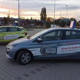 Dwa samochody z oznaczeniami szkoły nauki jazdy z Łodzi, zaparkowane na placu manewrowym. Na dachu niebieskiego auta widoczna tabliczka z literą 'L'.