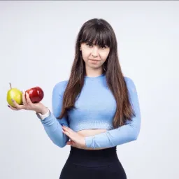 Kobieta w sportowym stroju trzymająca w dłoni jabłko i gruszkę na białym tle, prezentacja zdrowej diety.