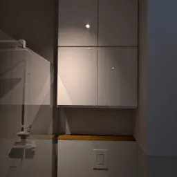 Wysoka szafka kuchenna z czterema białymi, błyszczącymi frontami, zamontowana nad blatem z jasnego drewna, widoczny włącznik światła na ścianie poniżej.