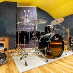 Czarny zestaw perkusyjny Pearl w profesjonalnym studio nagrań z panelami akustycznymi i kolumnami głośnikowymi.