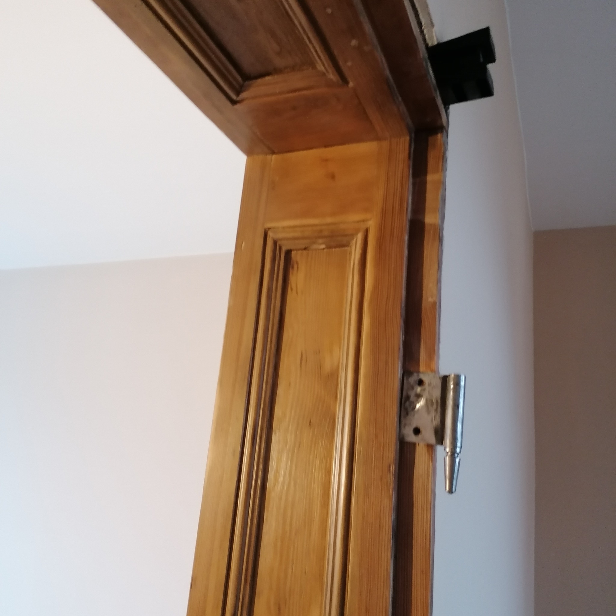 Fragment odnowionej, drewnianej ościeżnicy z widocznymi zawiasami, zamontowanej w odnowionym wnętrzu.