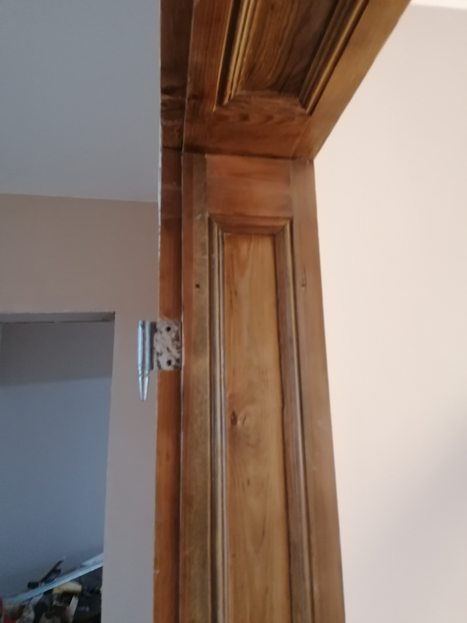 Drewniana ościeżnica z zamontowanym zawiasem drzwiowym, widoczne ślady po wcześniejszym montażu, wnętrze w trakcie remontu.