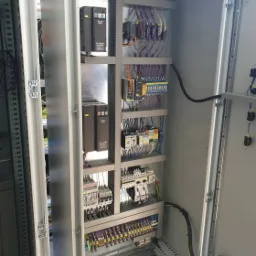 Otwarta szafa sterownicza z zainstalowanymi modułami, okablowaniem i zabezpieczeniami, widoczne brązowe falowniki Delta Electronics na metalowej płycie montażowej.