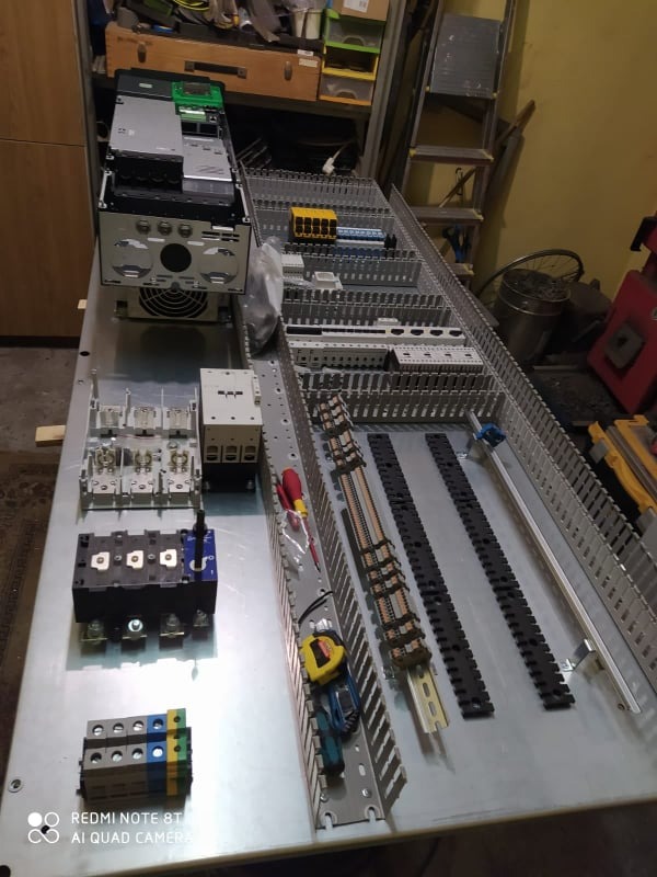 Rozdzielnica elektryczna w trakcie montażu, widoczne zabezpieczenia, listwy zaciskowe, przewody oraz narzędzia na metalowej płycie montażowej.