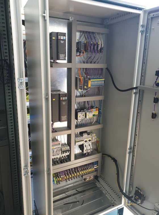 Otwarta szafa sterownicza z zainstalowanymi modułami, okablowaniem i zabezpieczeniami, widoczne brązowe falowniki Delta Electronics na metalowej płycie montażowej.