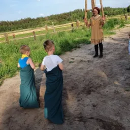 Dwaj chłopcy w workach do skakania, na tle animator w kostiumie indiańskim i drewniana konstrukcja na polanie.