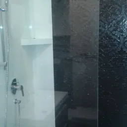 Nowoczesna kabina prysznicowa z czarno-białymi płytkami, widoczna deszczownica i bateria, z dekoracyjną czarną ścianą z motywem roślinnym.