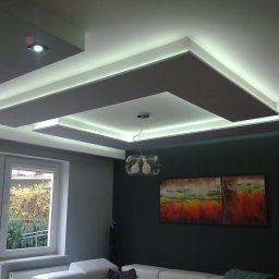 Mark.Kom Rafał Klementowski - Nowoczesny salon z podwieszanym sufitem z oświetleniem LED, szare ściany, okno z widokiem na ogród, abstrakcyjny obraz na ścianie.