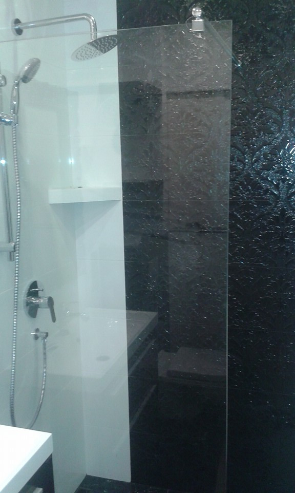 Nowoczesna kabina prysznicowa z czarno-białymi płytkami, widoczna deszczownica i bateria, z dekoracyjną czarną ścianą z motywem roślinnym.