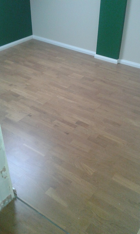 Ułożony parkiet w pokoju z zielonymi i kremowymi ścianami, widoczny fragment ściany z resztkami kleju po remoncie.