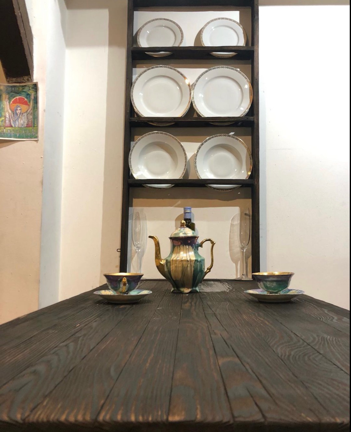 Ciemny drewniany stół z zastawą stołową: dzbanek, filiżanki i talerze w tle na półce.
