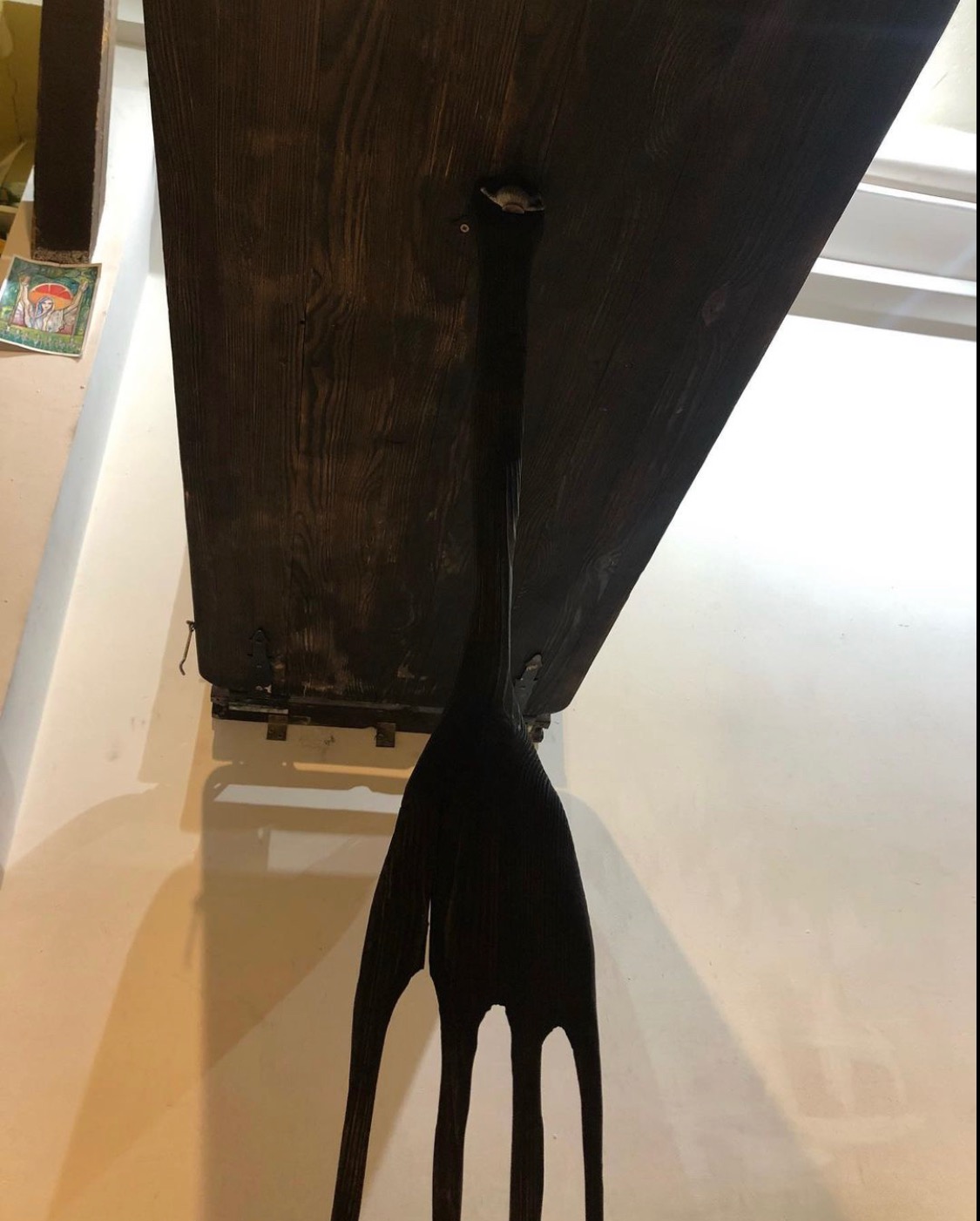 Ciemnobrązowy, drewniany blat stołu przymocowany do ściany za pomocą metalowych wsporników i ozdobnej, drewnianej nogi w stylu retro z czterema smukłymi odnogami.