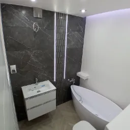 Nowoczesna łazienka z owalną wanną, wiszącą szafką z umywalką i marmurowymi płytkami z podświetleniem LED, na podłodze parkiet ułożony w jodełkę.