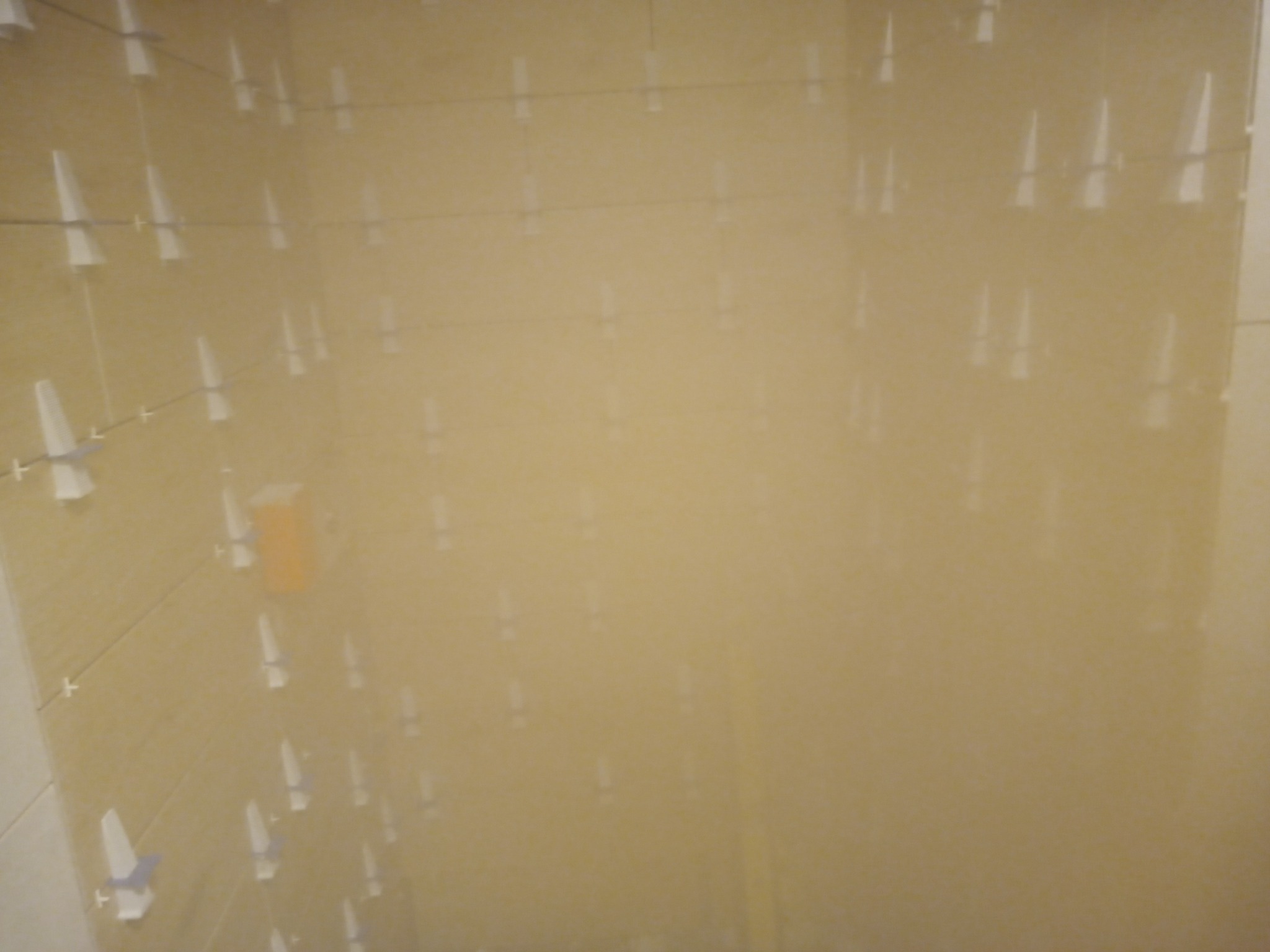 Świeżo położone, beżowe płytki ścienne z krzyżykami dystansowymi i poziomnicą, widoczne na ścianie w trakcie prac glazurniczych.