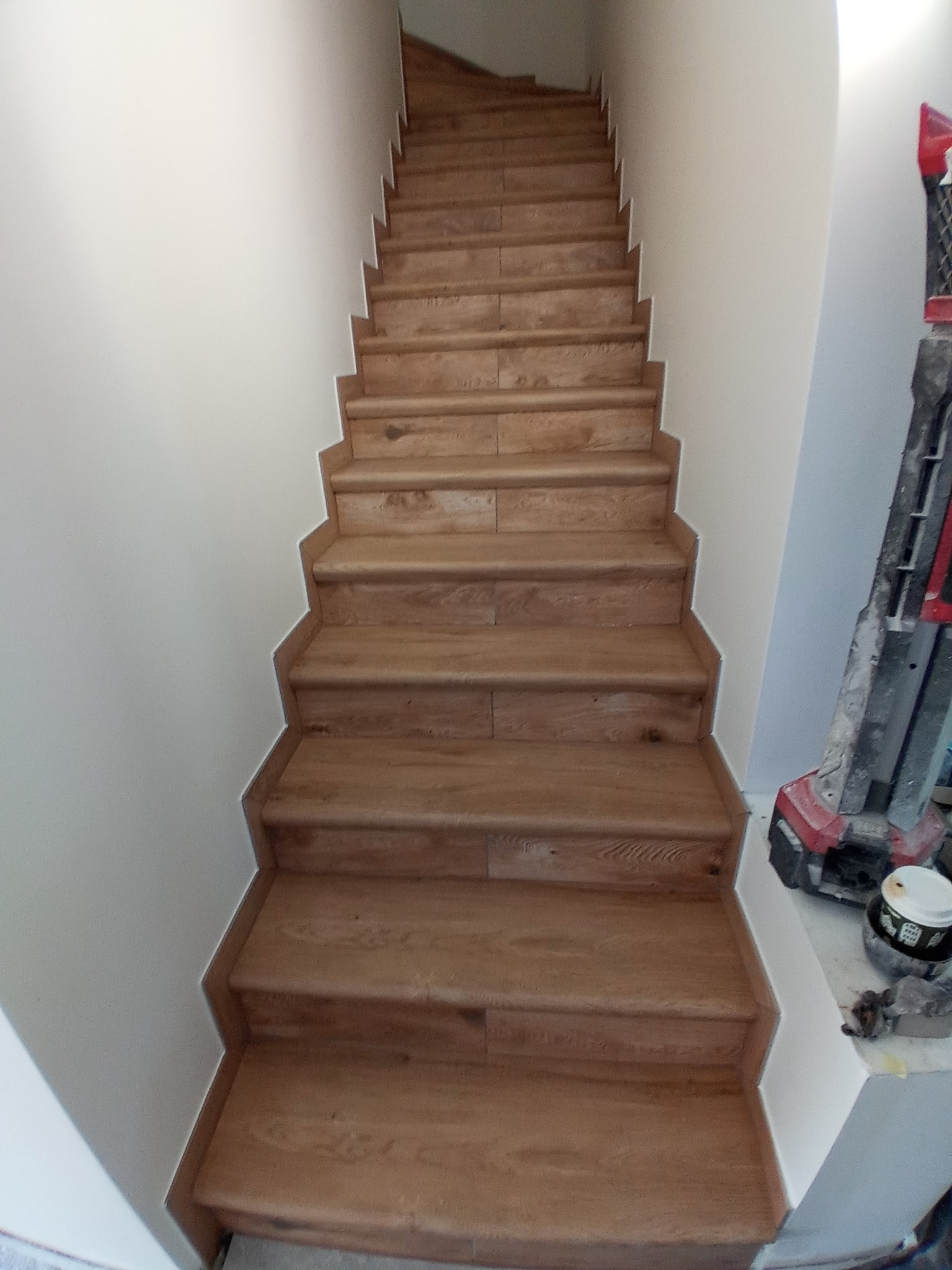 Schody wyłożone płytkami imitującymi drewno, widok z dołu, przy ścianie widoczny sprzęt budowlany.