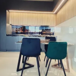 Nowoczesna kuchnia z drewnianymi szafkami g&oacute;rnymi z podświetleniem LED, szarymi szafkami dolnymi, blatem imitującym marmur i szklanym panelem z widokiem na miasto, uzupełniona o st&oacute;ł z marmurowym...