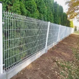 Białe, metalowe ogrodzenie panelowe z podmurówką betonową, widok z boku na tle wysokich, zielonych tuj.