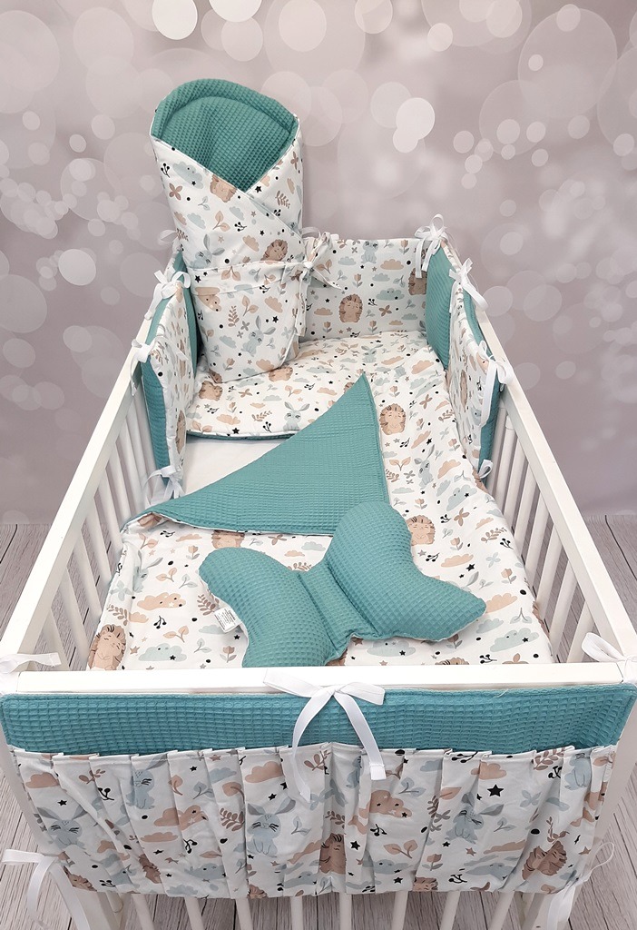 Komplet pościeli do łóżeczka dziecięcego z motywem zwierząt, w skład którego wchodzi ochraniacz na szczebelki, kołderka, poduszka motylek i rożek, utrzymany w kolorystyce bieli, beżu i turkusu.