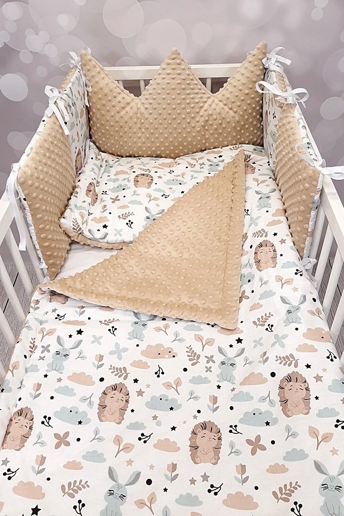 Komplet pościeli do łóżeczka dziecięcego z motywem jeży i królików, beżowe ochraniacze z wypustkami w kształcie korony, białe sznurki do wiązania, widok z góry.