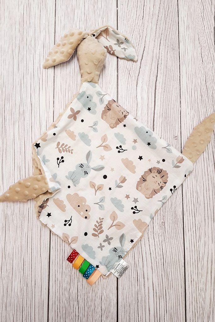 Dziecięca przytulanka w kształcie królika z miękkiego materiału z wypustkami i wzorem w zwierzątka na białym tle drewnianych desek.