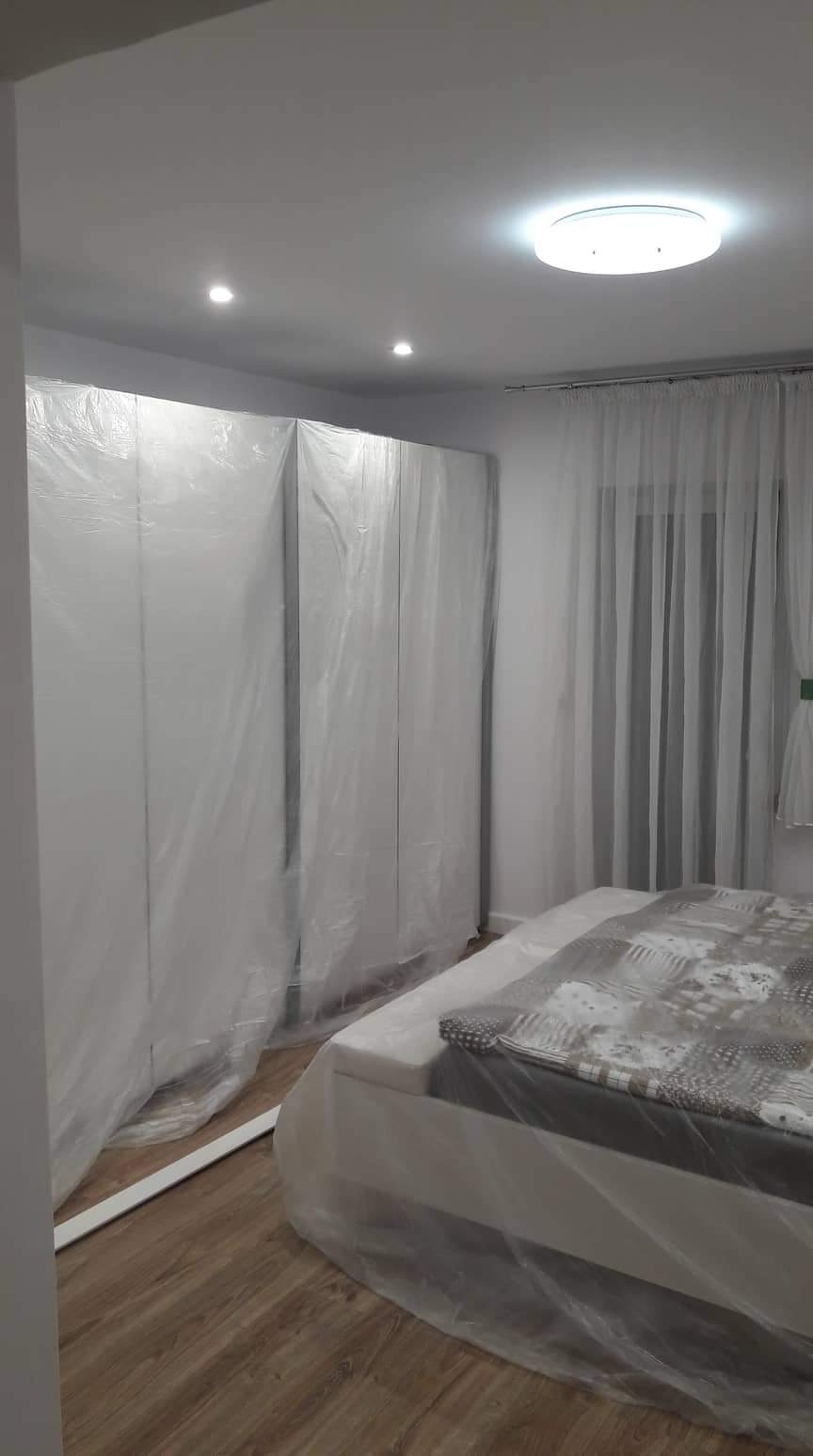 Pokój w trakcie zabezpieczania folią malarską: szafa wnękowa i łóżko przykryte folią ochronną, parkiet na podłodze.