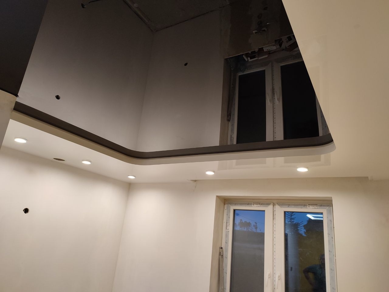 Wykończone wnętrze z błyszczącym, podwieszanym sufitem z oświetleniem punktowym, widoczne okno w ścianie i odbicie w suficie.