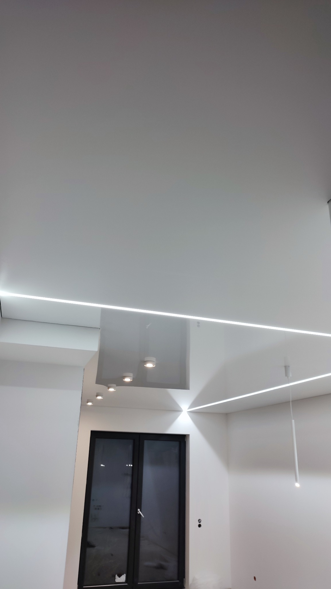 Nowoczesne oświetlenie sufitowe z liniami LED i punktowymi lampami w pomieszczeniu z czarnymi drzwiami balkonowymi.