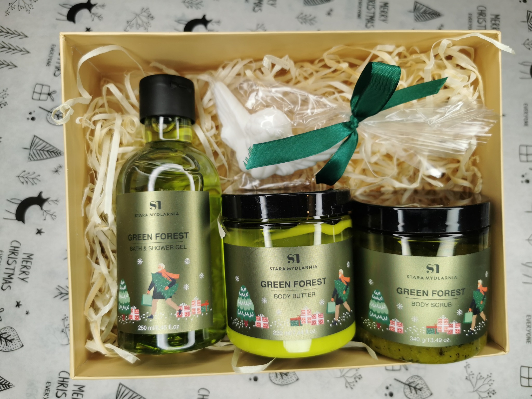 Świąteczny zestaw kosmetyków 'Green Forest' marki Stara Mydlarnia w beżowym pudełku wypełnionym siankiem, zawierający żel do kąpieli, masło do ciała i peeling, uzupełniony mydełkiem w kształcie...