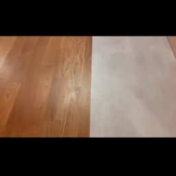 Kosmiczne Remonty - Fragment podłogi: połowa wykończona lakierowanym parkietem, druga połowa pokryta świeżo wylaną, jasną wylewką samopoziomującą, widoczne przejście między materiałami.