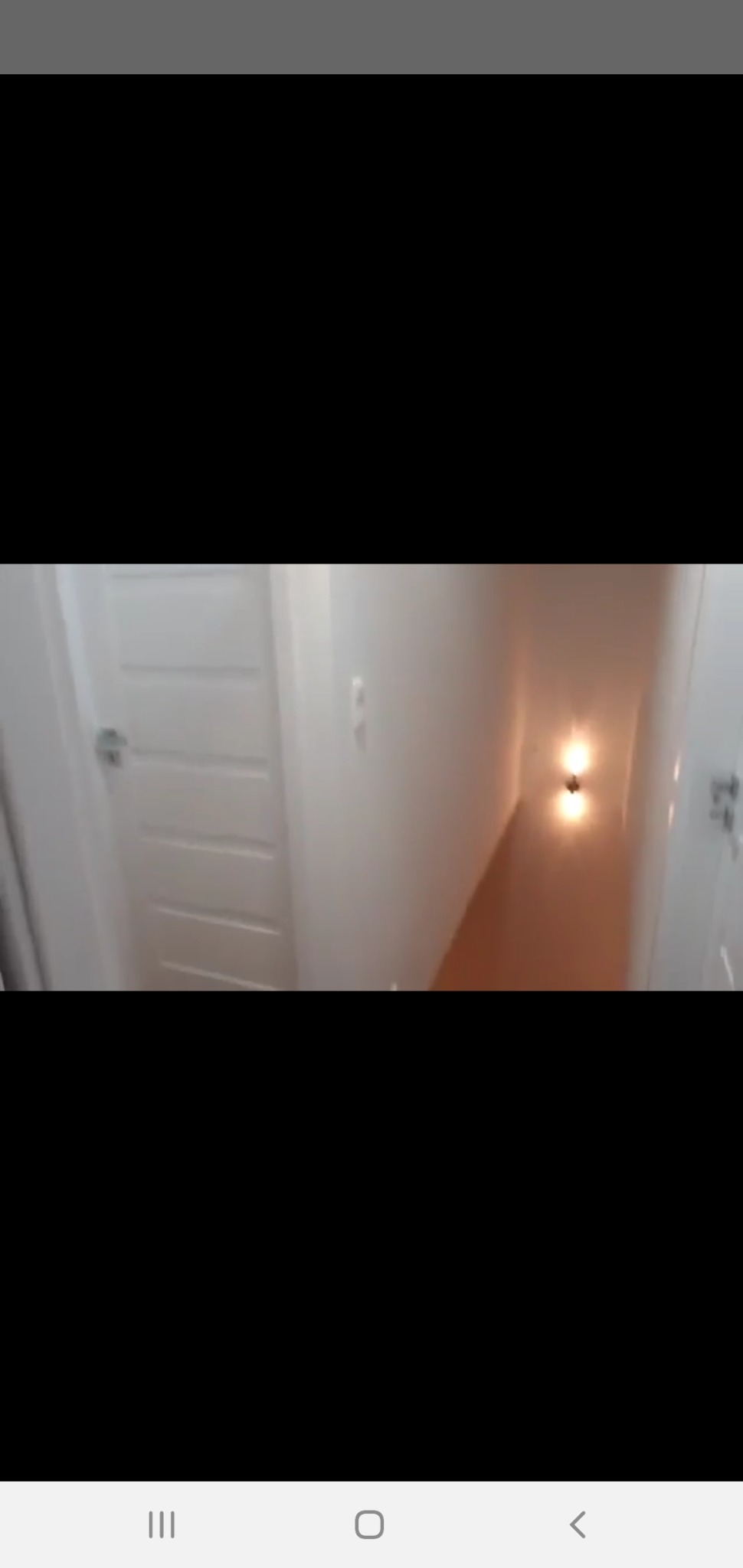 Korytarz po remoncie z białymi ścianami, drewnianą podłogą i dwoma kinkietami o ciepłej barwie światła, widok z perspektywy wejścia.