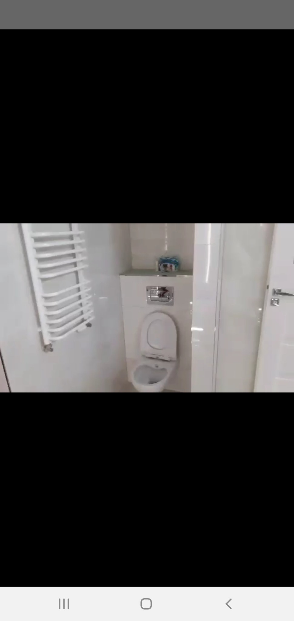 Biała, błyszcząca łazienka po remoncie, widoczna toaleta z otwartą klapą, grzejnik drabinkowy i częściowo widoczne drzwi, na półce nad toaletą leżą rolki papieru toaletowego.