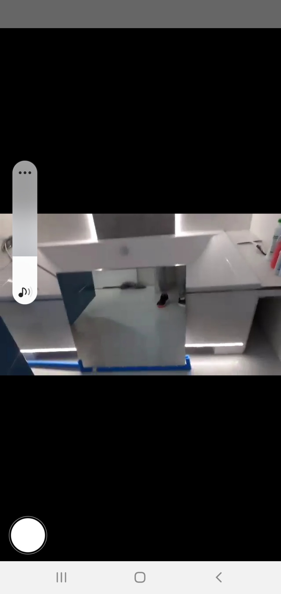 Nowoczesna, biała umywalka z podświetleniem LED, widoczna w lustrze odbijającym fragment podłogi i stopy osoby w sportowych butach.