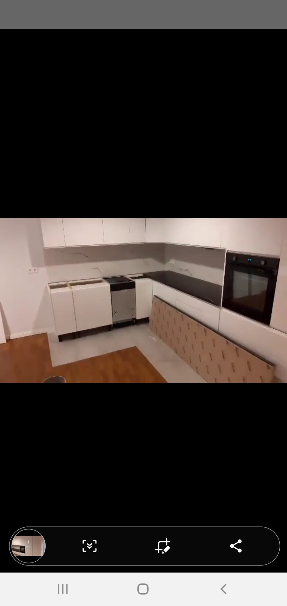 Wnętrze kuchni w trakcie montażu: białe szafki bez frontów, czarny blat, płyta meblowa oparta o ścianę, widoczna zmywarka i piekarnik.