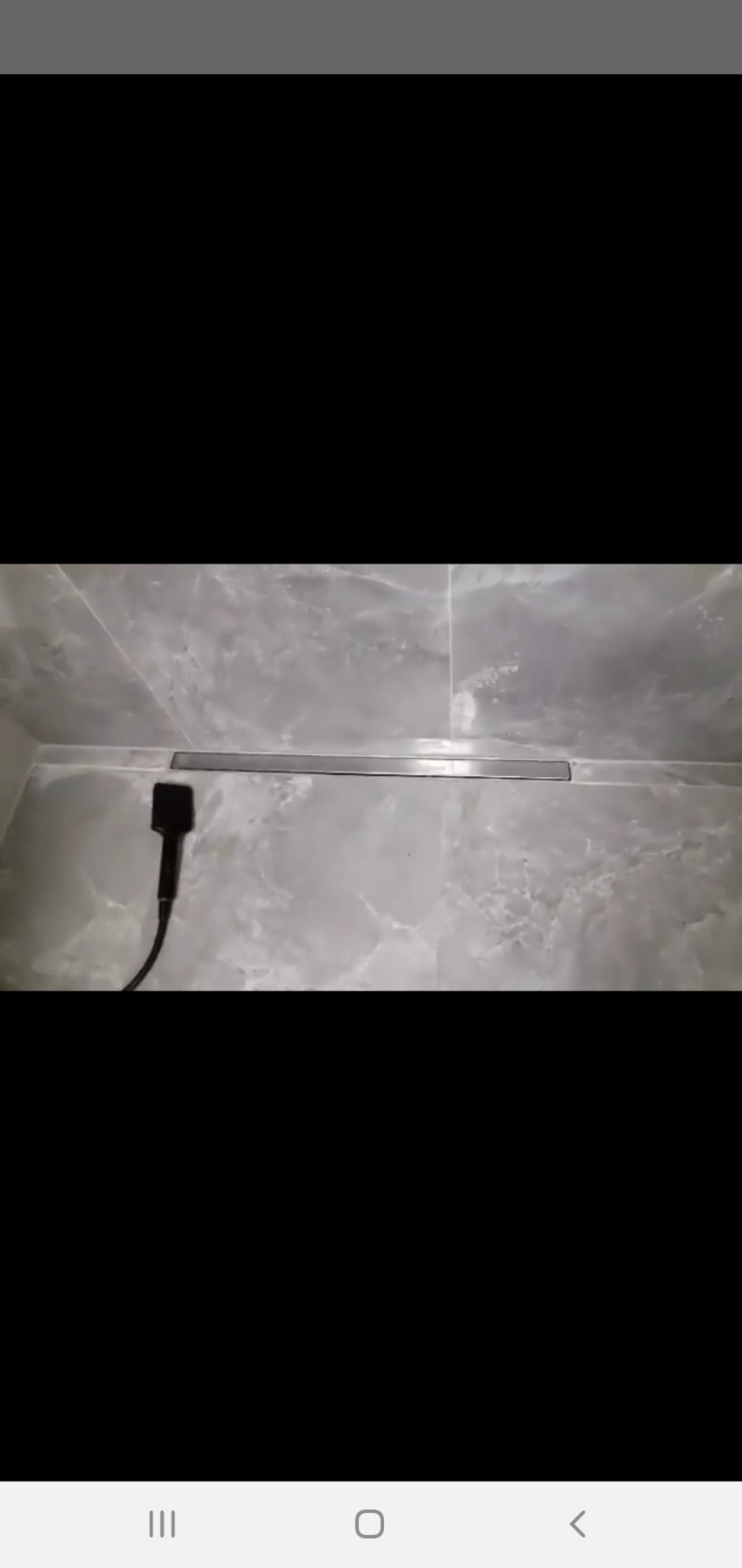 Szary, marmurkowy kafel z odpływem liniowym i czarną słuchawką prysznicową z kablem.