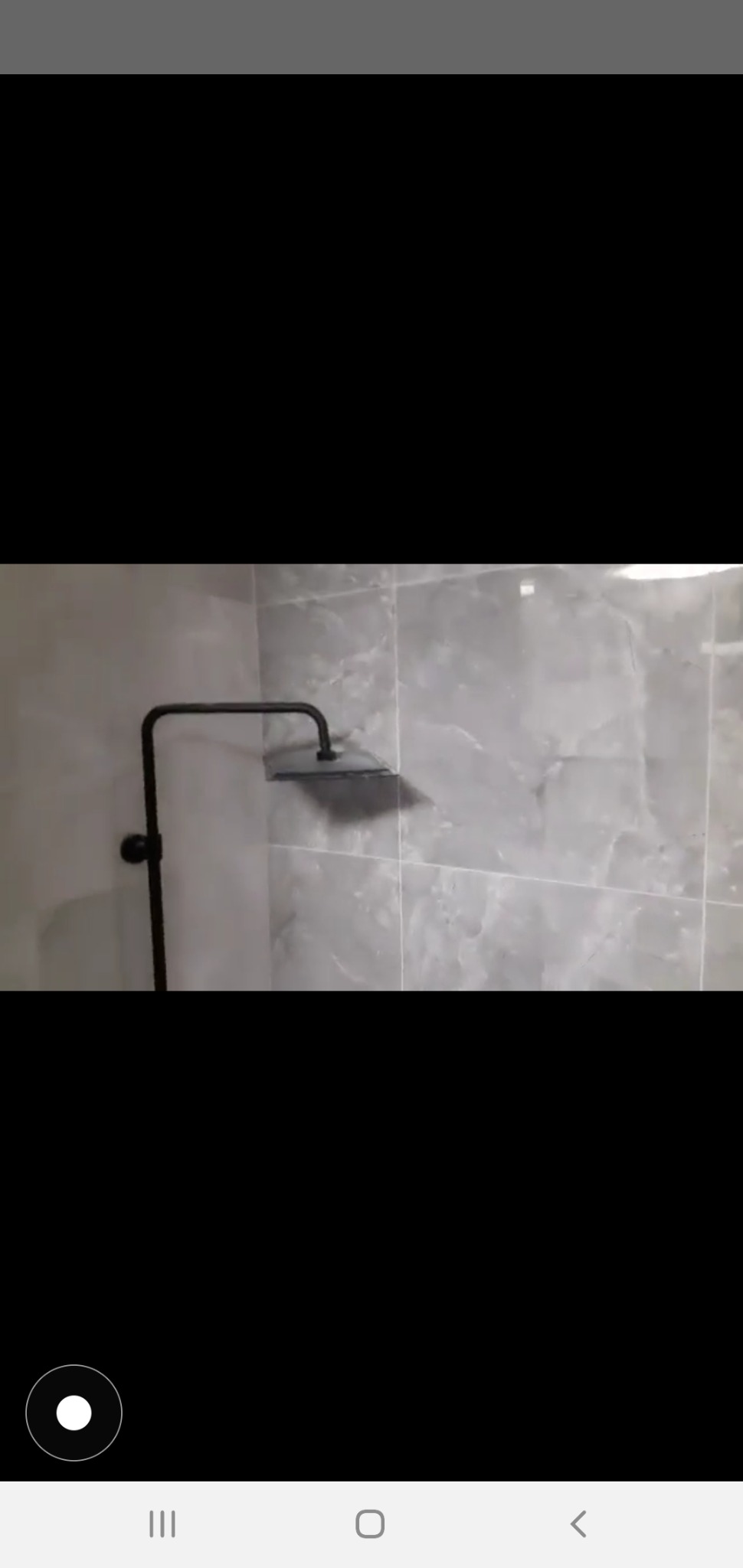 Czarny, nowoczesny zestaw prysznicowy zamontowany na ścianie wyłożonej szarymi płytkami imitującymi marmur.